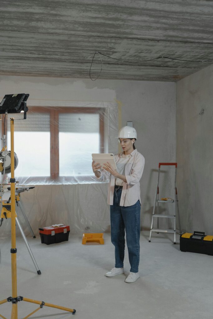 Woman in construction helmet reviewing plans on a tablet at an indoor renovation site.